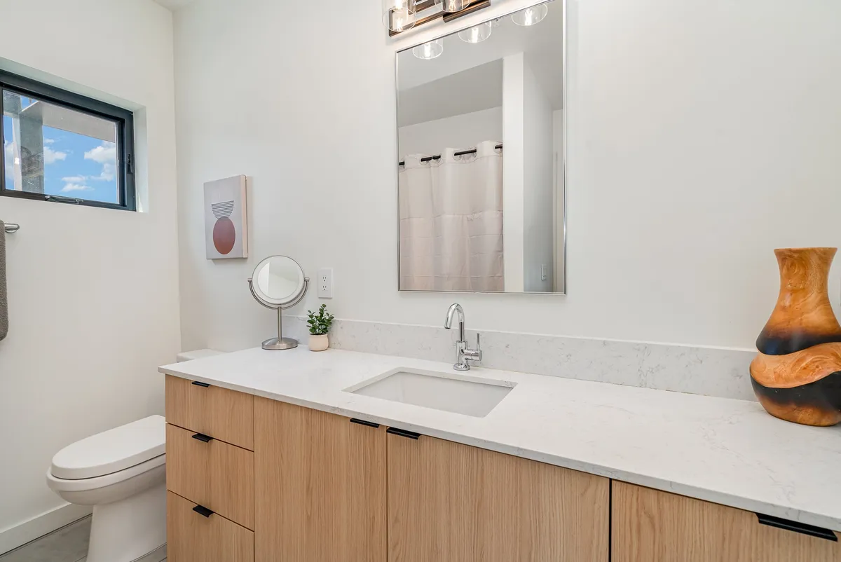 A modern bathroom with a sleek vanity, large mirror, decorative vase, and contemporary wall art. The space is bright and fresh, designed for relaxation and stylish self-care routines.