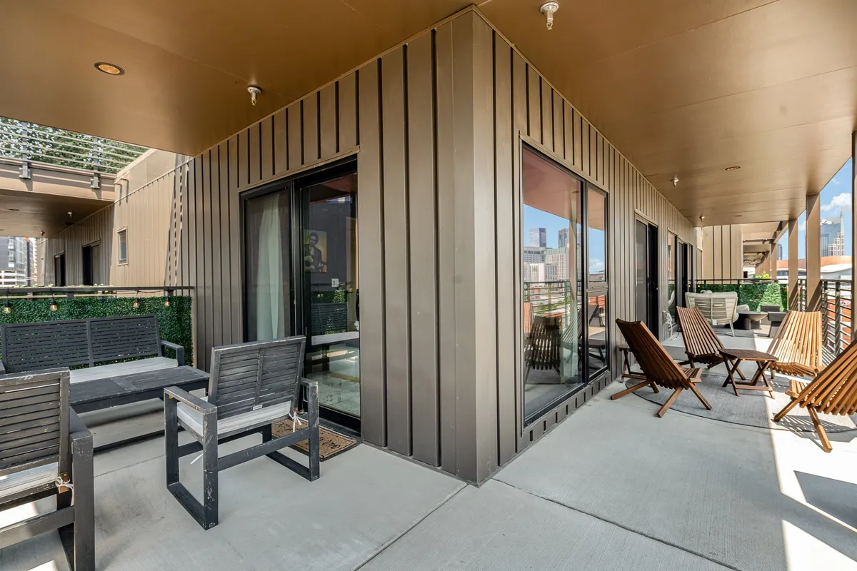 A private patio featuring comfortable outdoor seating, large windows, and a sweeping city skyline view. The arrangement suggests a space ideal for socializing or lounging while taking in the urban atmosphere.