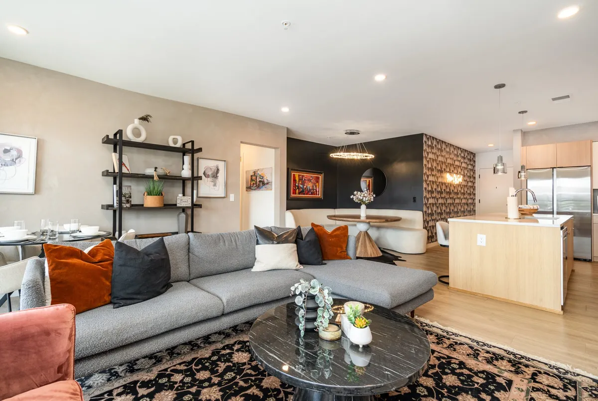 This image captures a spacious, open-concept interior with a large sectional sofa, a round coffee table, a clear view of the dining area, and a kitchen island beyond. The arrangement encourages social gatherings, lounging, and entertaining, with easy flow between the living, dining, and kitchen spaces.