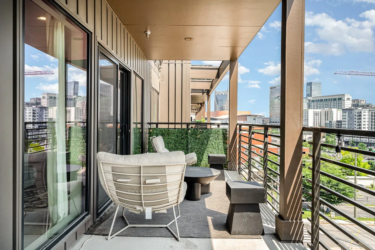 A contemporary balcony scene with cozy seating, a greenery wall, and expansive views of the city, creating an inviting spot for relaxing or socializing while taking in the Nashville skyline.