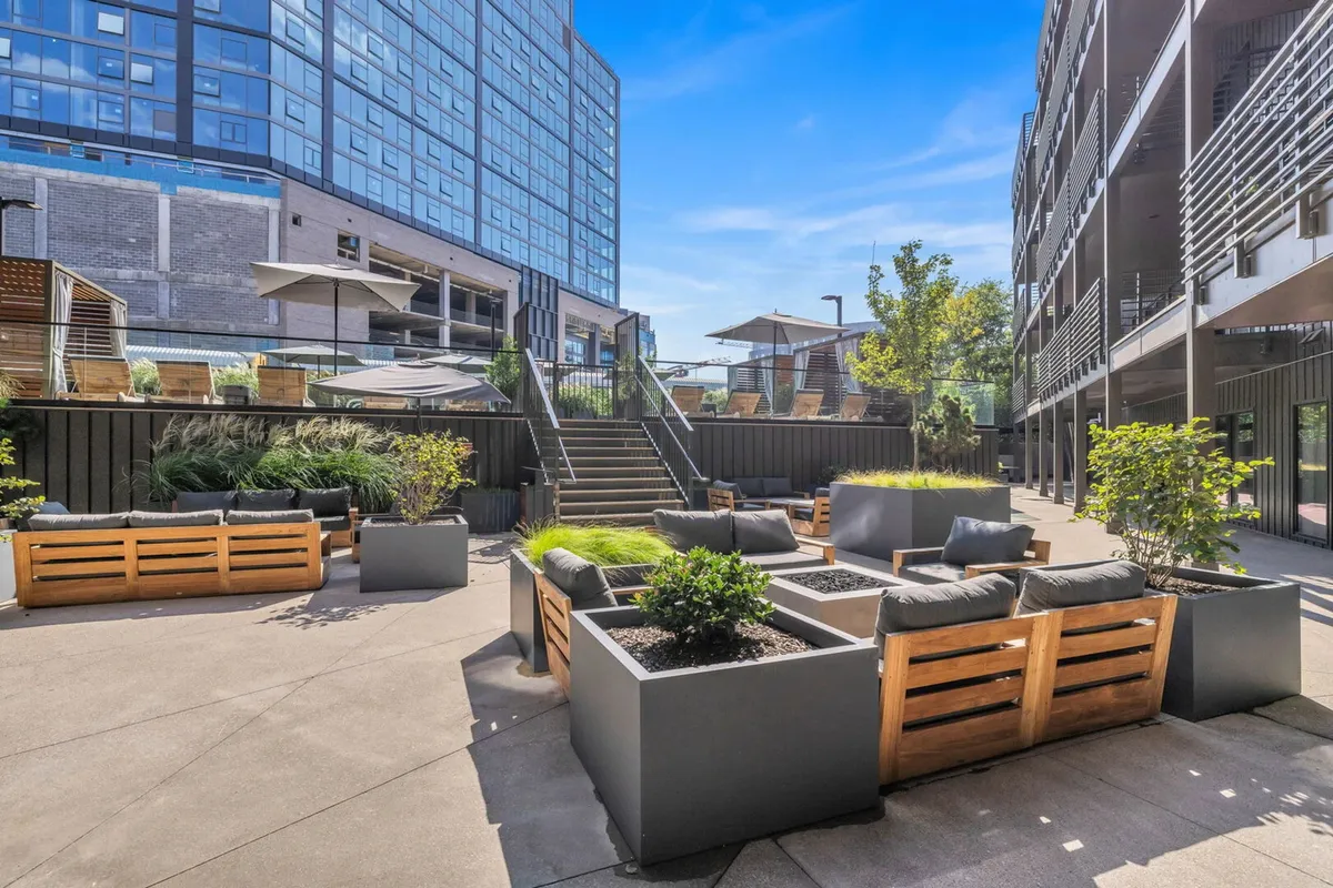 A contemporary rooftop area with modern seating, planters, and a canopy-covered lounge. The rooftop offers ample space for gatherings, sunset viewing, and cityscape relaxation, reinforcing the social aspect of Hyve living.