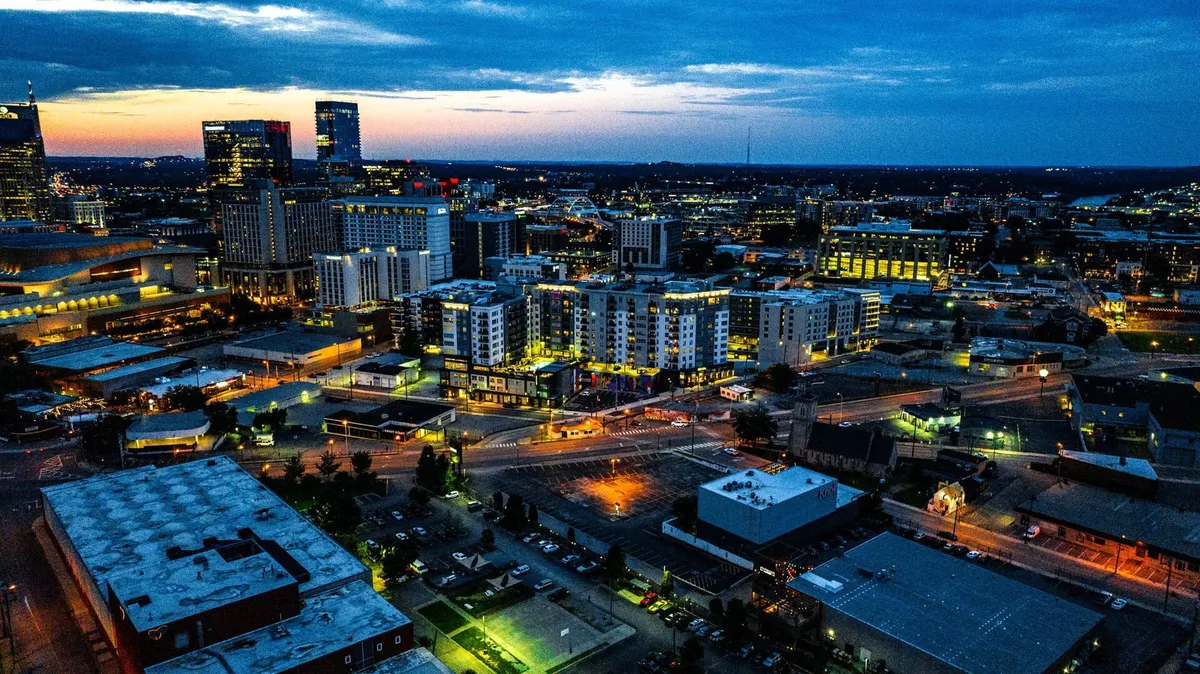 A dynamic city skyline at dusk, illuminated buildings, busy streets, and cars, capturing the urban energy and vibrancy of downtown Nashville.