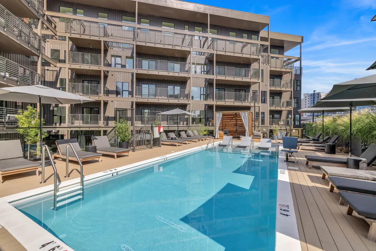 A bright exterior shot of the community’s family-friendly pool area, complete with a sparkling swimming pool, lounge chairs, balconies, and lush landscaping. The inviting atmosphere suggests relaxation and fun for all ages.