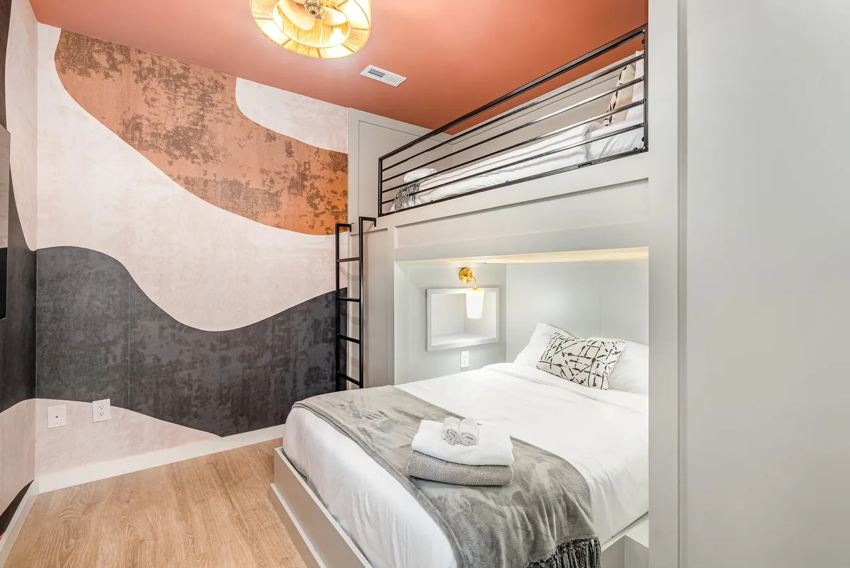 A stylish bunk room featuring a modern bunk bed design, decorative wall art, and warm ambient lighting. The room feels cozy and inviting, perfect for kids or friends to share a restful space.